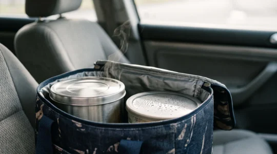 Sac de transport isotherme ouvert laissant apparaitre un contenant en inox entoure de vapeur legere, symbolisant la conservation de la chaleur pendant le trajet